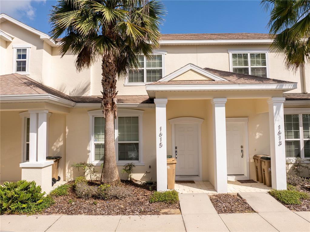 A two-story townhouse exterior features a palm tree, two front entrances, and beige siding — 1615 RETREAT CIRCLE, CLERMONT, FL