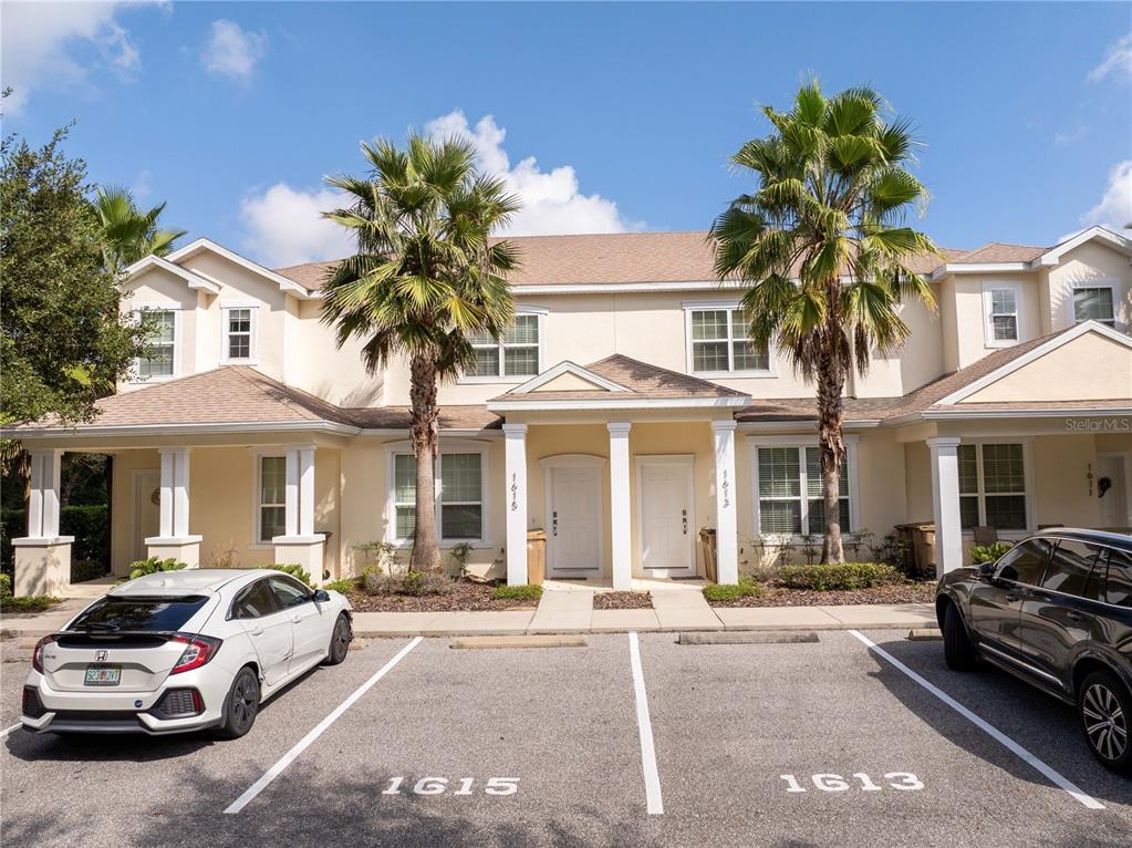 A two-story townhouse exterior features two white front doors, palm trees, and assigned parking spaces — 1615 RETREAT CIRCLE, CLERMONT, FL