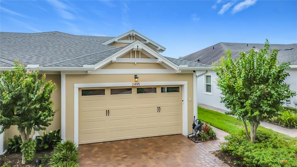 A tan house exterior features a two-car garage with windows and a paved driveway — 2495 DATURA LOOP, ST CLOUD, FL