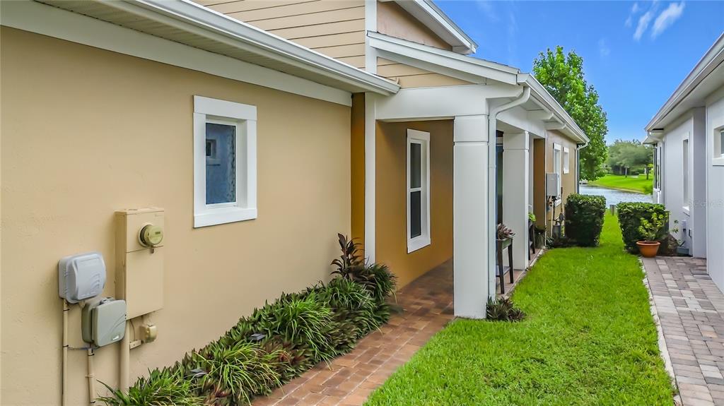 A side view of a house exterior featuring a paved walkway, landscaping, and utility boxes — 2495 DATURA LOOP, ST CLOUD, FL