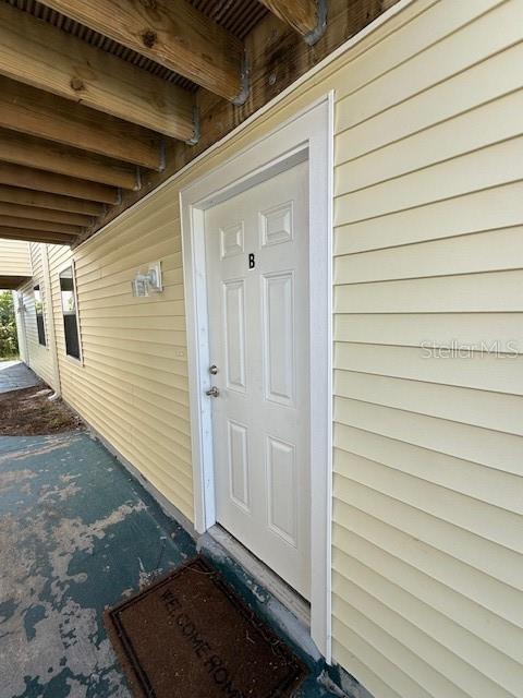 A white door labeled B is set into a yellow-sided exterior wall under a wooden deck — 140 HUNTER LAKE DRIVE UNIT B, OLDSMAR, FL
