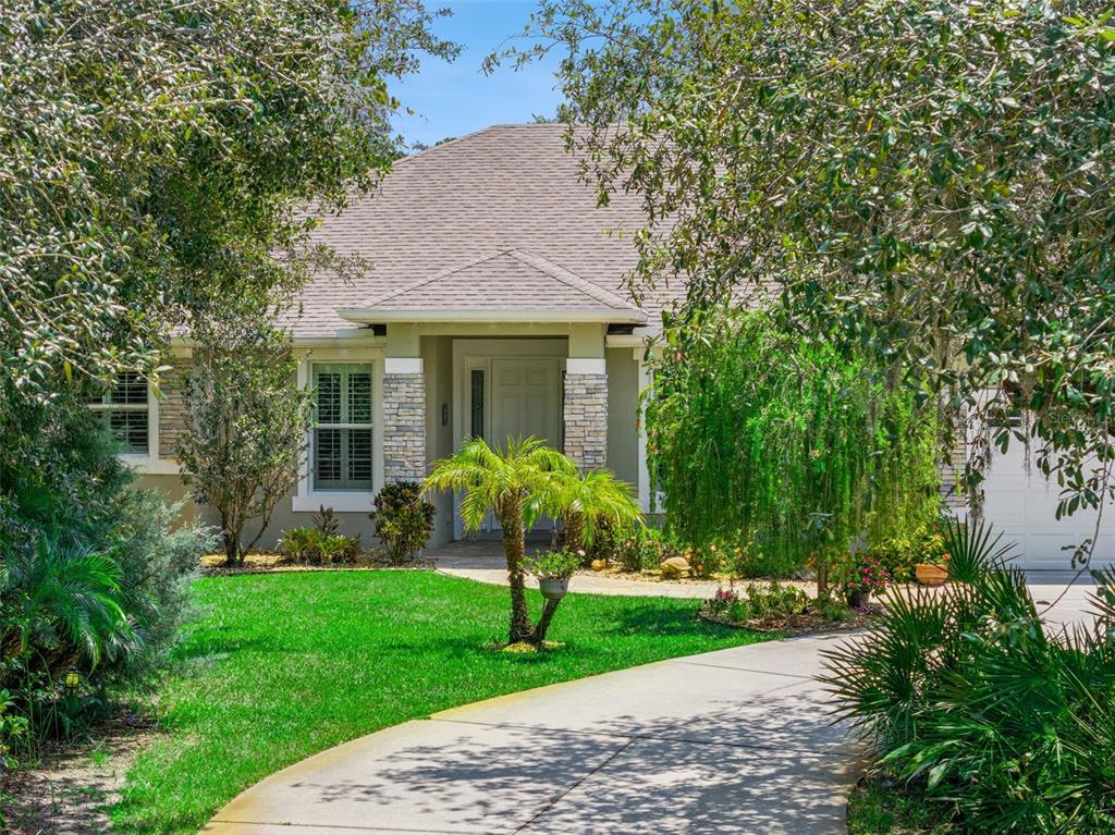 A single-story house with a stone-accented entryway, a concrete driveway, and lush landscaping — 11540 NELLIE OAKS BEND, CLERMONT, FL