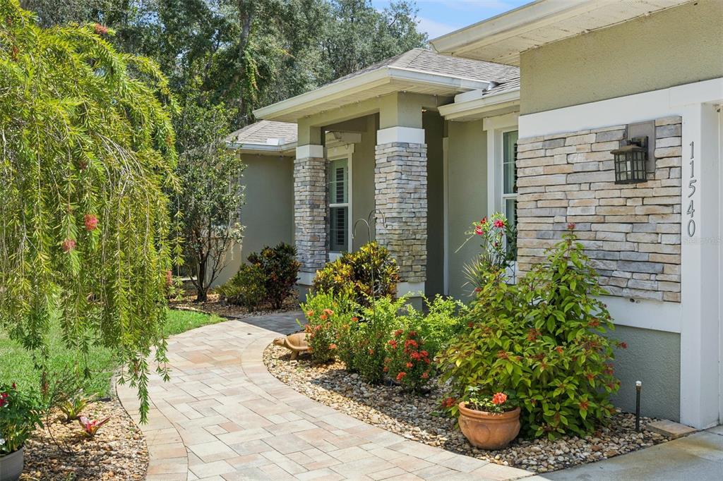 A paved walkway leads to the front entrance of a house with stone pillar accents — 11540 NELLIE OAKS BEND, CLERMONT, FL