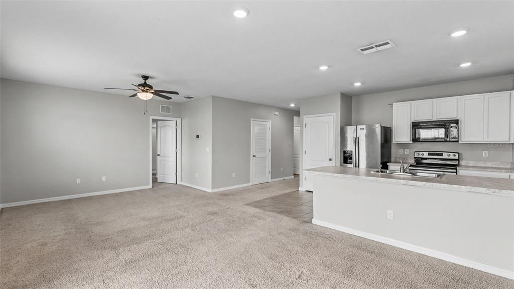 An open-concept living area features beige carpeting, a ceiling fan, and an adjacent kitchen — 524 BURNHAM CIRCLE, AUBURNDALE, FL