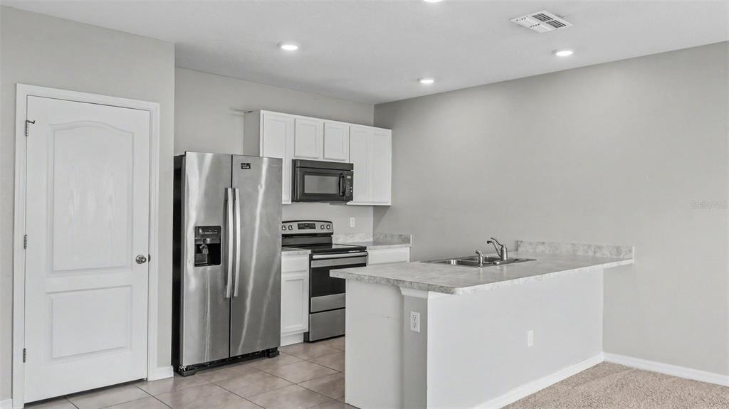 A kitchen features white cabinets, stainless steel appliances, and a peninsula with a sink — 524 BURNHAM CIRCLE, AUBURNDALE, FL