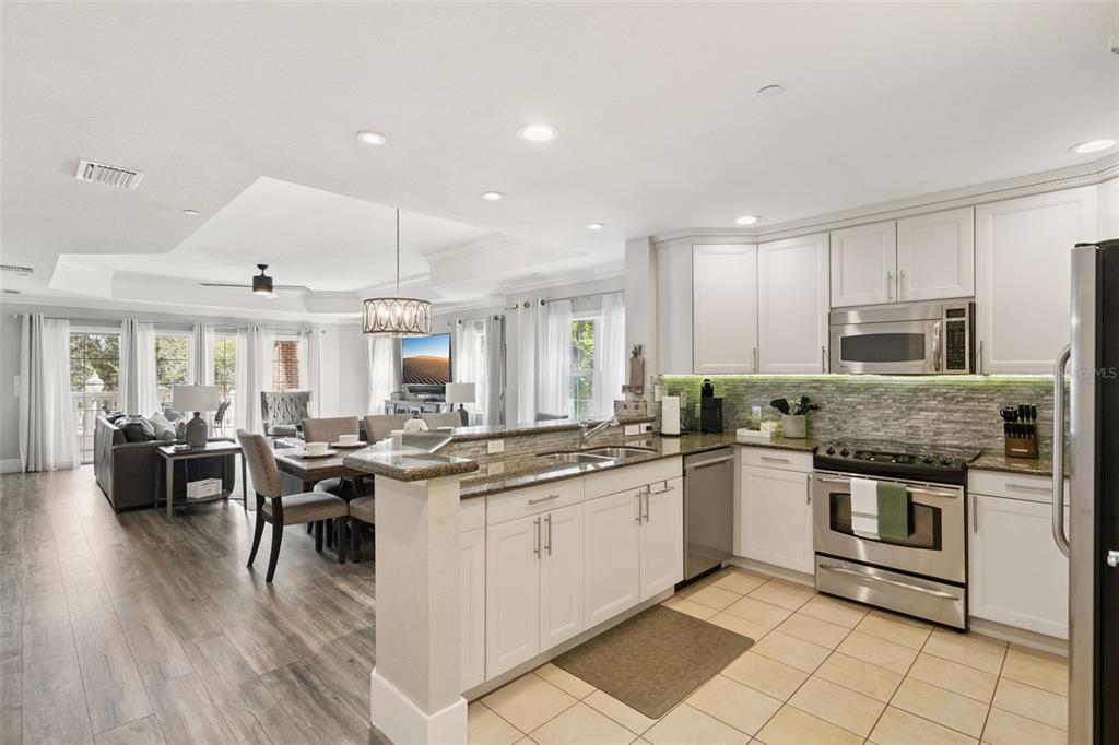 An open-concept kitchen with white cabinets and granite countertops overlooks a dining and living area — 7651 WHISPER WAY UNIT 204, REUNION, FL