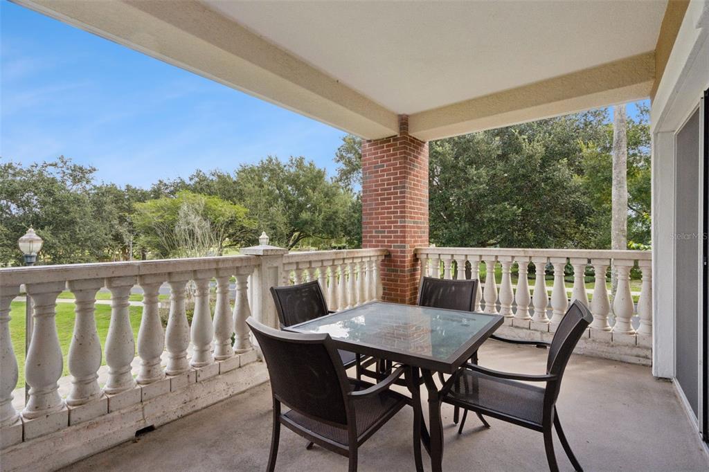 A covered balcony features a glass-top table with four chairs and a stone balustrade railing — 7651 WHISPER WAY UNIT 204, REUNION, FL