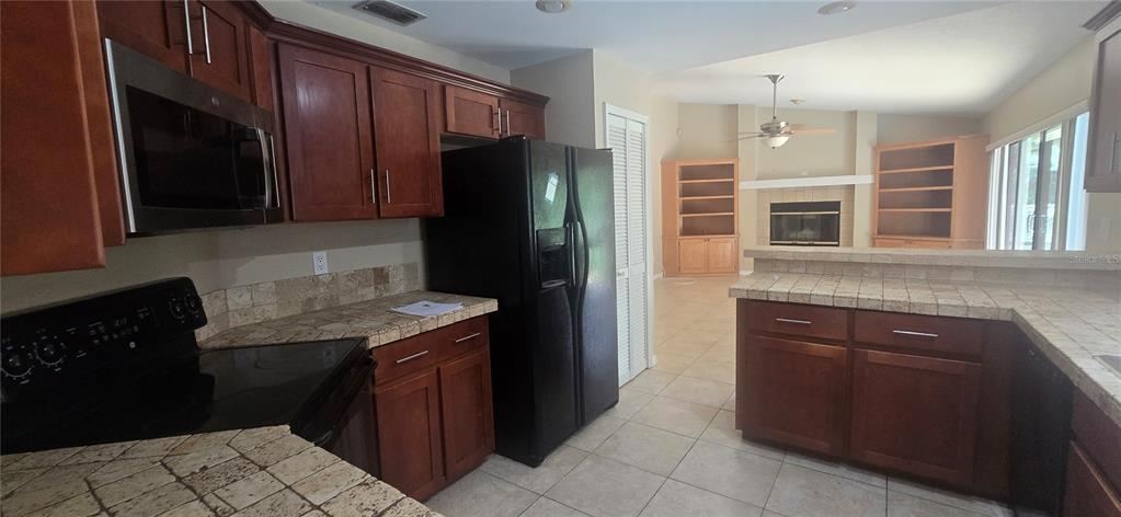 A kitchen with dark wood cabinets, black appliances, and tiled countertops opens to a living area — 1142 ODAY DRIVE, WINTER SPRINGS, FL