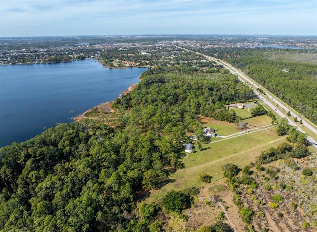 An aerial view shows a wooded property bordering a lake next to a highway — 8834 WINTER GARDEN VINELAND ROAD, ORLANDO, FL