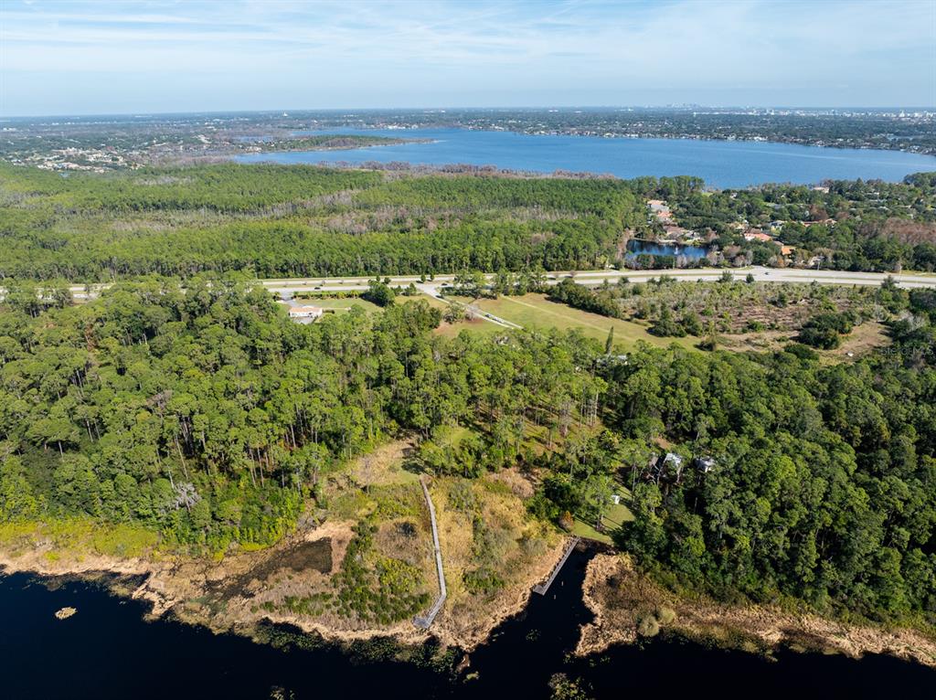 An aerial view shows a wooded property with a boardwalk leading to a lake — 8834 WINTER GARDEN VINELAND ROAD, ORLANDO, FL