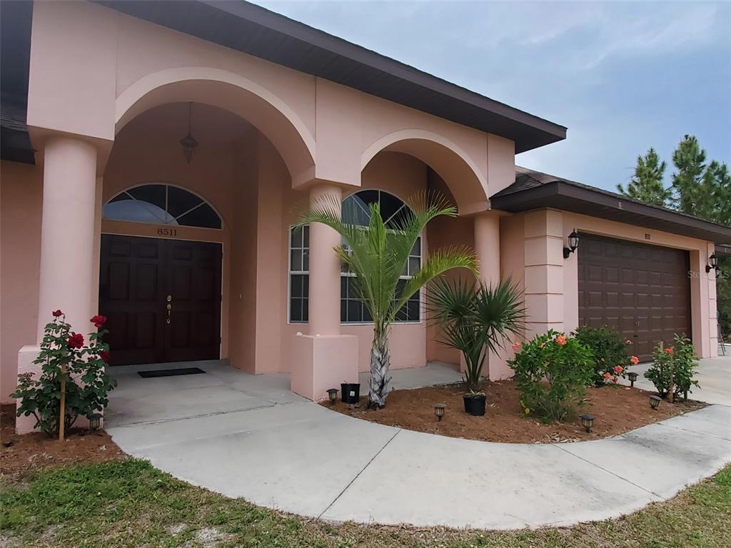 A peach-colored house features a covered entryway with arched columns and a brown garage door — 8511 AUSTRIAN BOULEVARD, PUNTA GORDA, FL