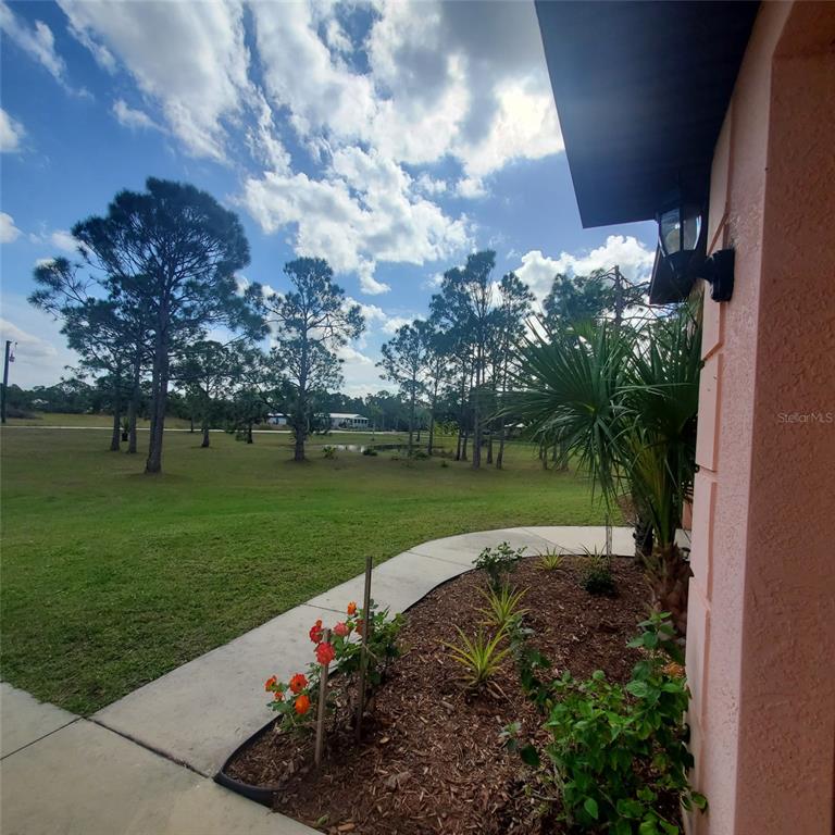 A view from a porch looking out over a grassy yard with trees and landscaping — 8511 AUSTRIAN BOULEVARD, PUNTA GORDA, FL