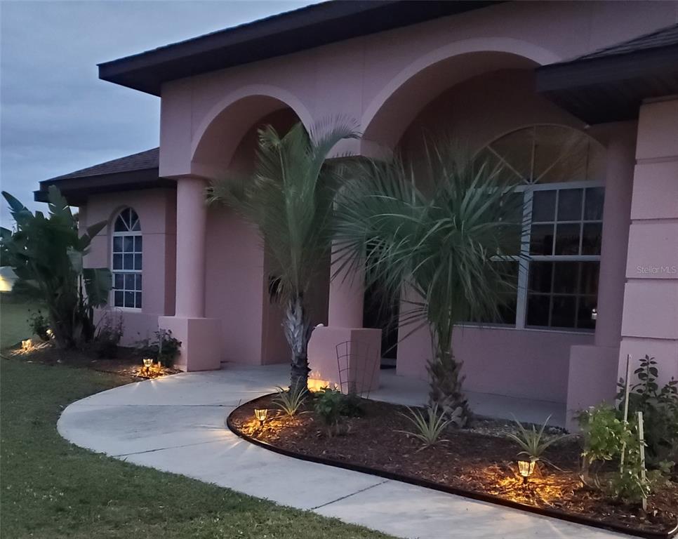 A pink stucco house features arched entryways, palm trees, and landscape lighting along a walkway — 8511 AUSTRIAN BOULEVARD, PUNTA GORDA, FL