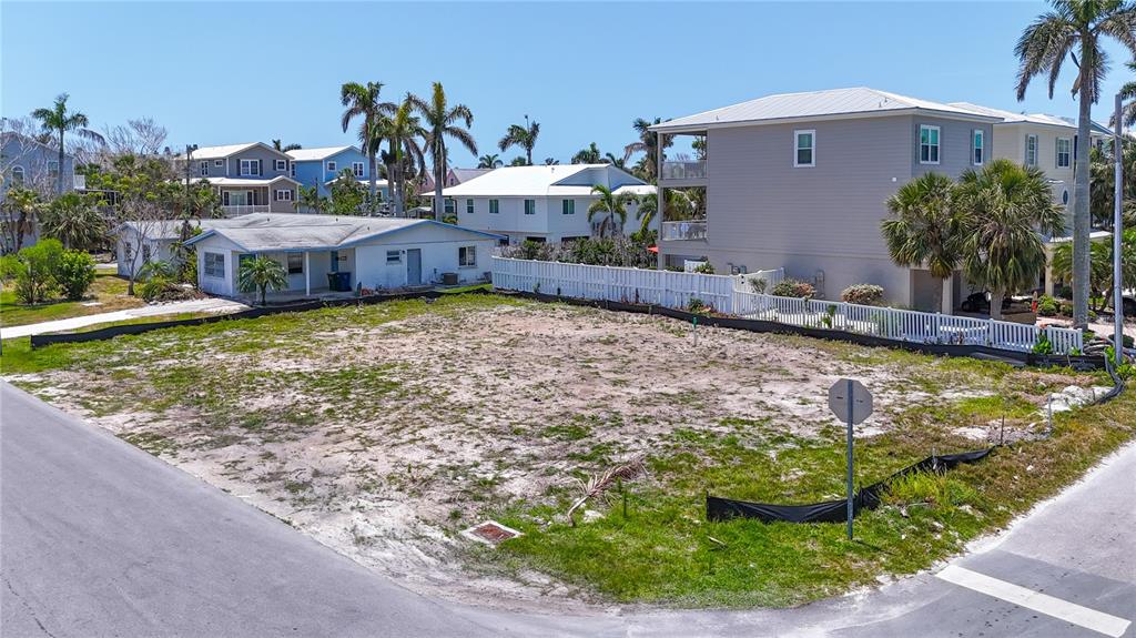 An empty, sandy residential lot sits between several houses under a clear blue sky — 6406 HOLMES BOULEVARD, HOLMES BEACH, FL