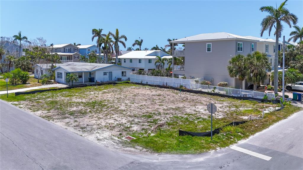 An empty, sandy residential lot sits on a corner street next to several houses — 6406 HOLMES BOULEVARD, HOLMES BEACH, FL