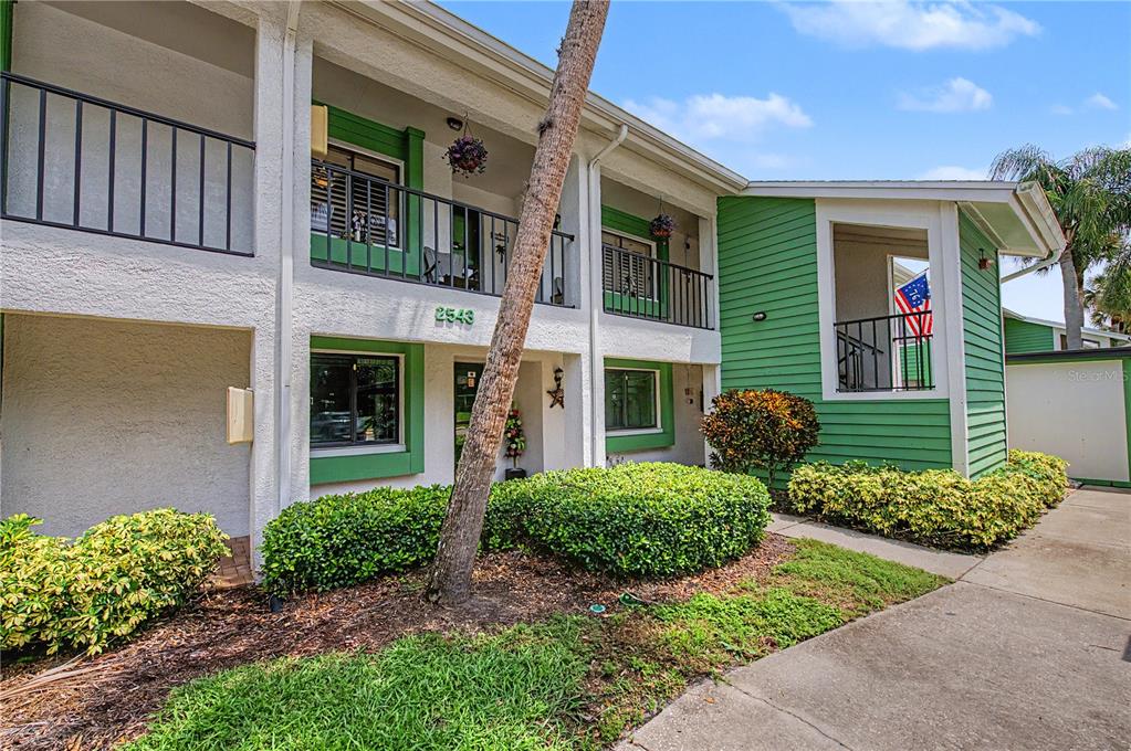 A two-story apartment building exterior features green siding, white stucco walls, and a palm tree — 2543 ROYAL PINES CIRCLE UNIT 17K, CLEARWATER, FL