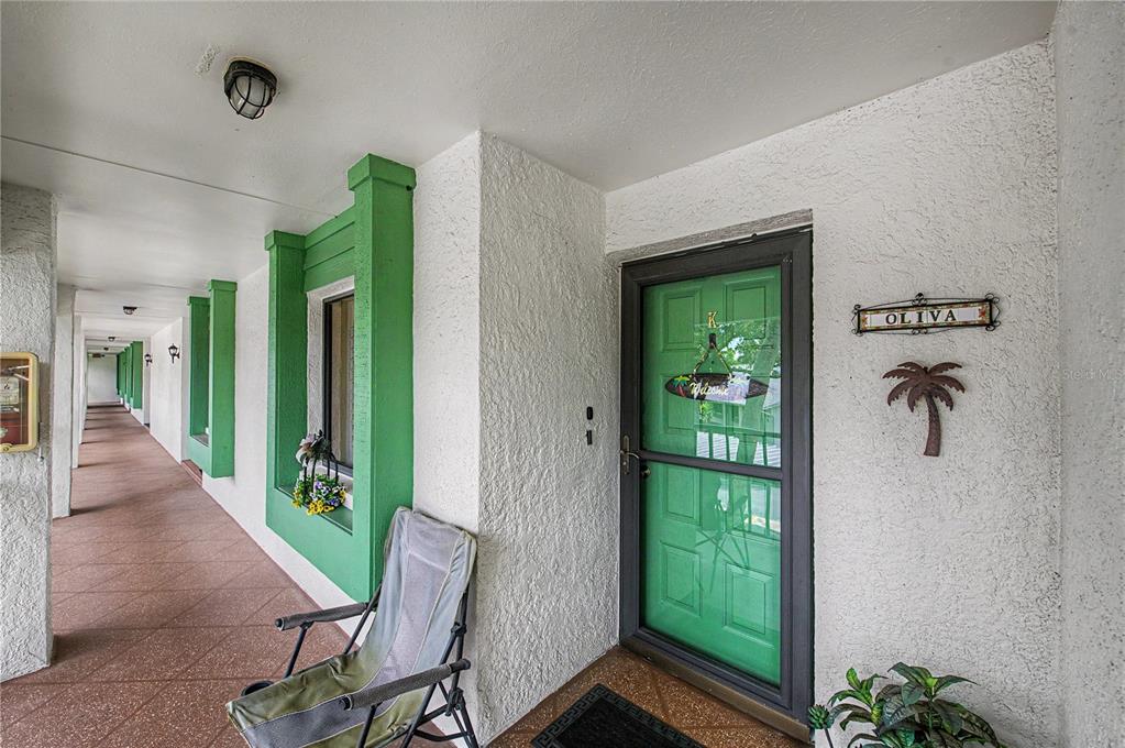 An exterior view of a residential building entrance with a green door and a chair — 2543 ROYAL PINES CIRCLE UNIT 17K, CLEARWATER, FL