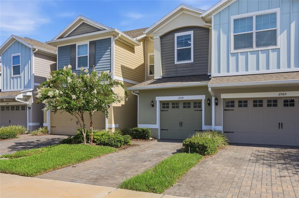 A row of three attached townhomes with paved driveways and garages under a blue sky — 2559 SEDGE GRASS WAY, ORLANDO, FL
