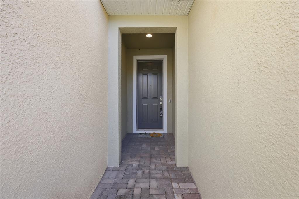 A recessed entryway features a dark gray front door, light stucco walls, and paver flooring — 2559 SEDGE GRASS WAY, ORLANDO, FL
