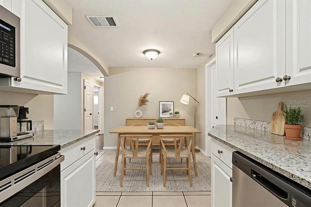 A kitchen with white cabinets and granite countertops opens into a dining area with wood furniture — 3319 CANTRELL STREET, HOLIDAY, FL