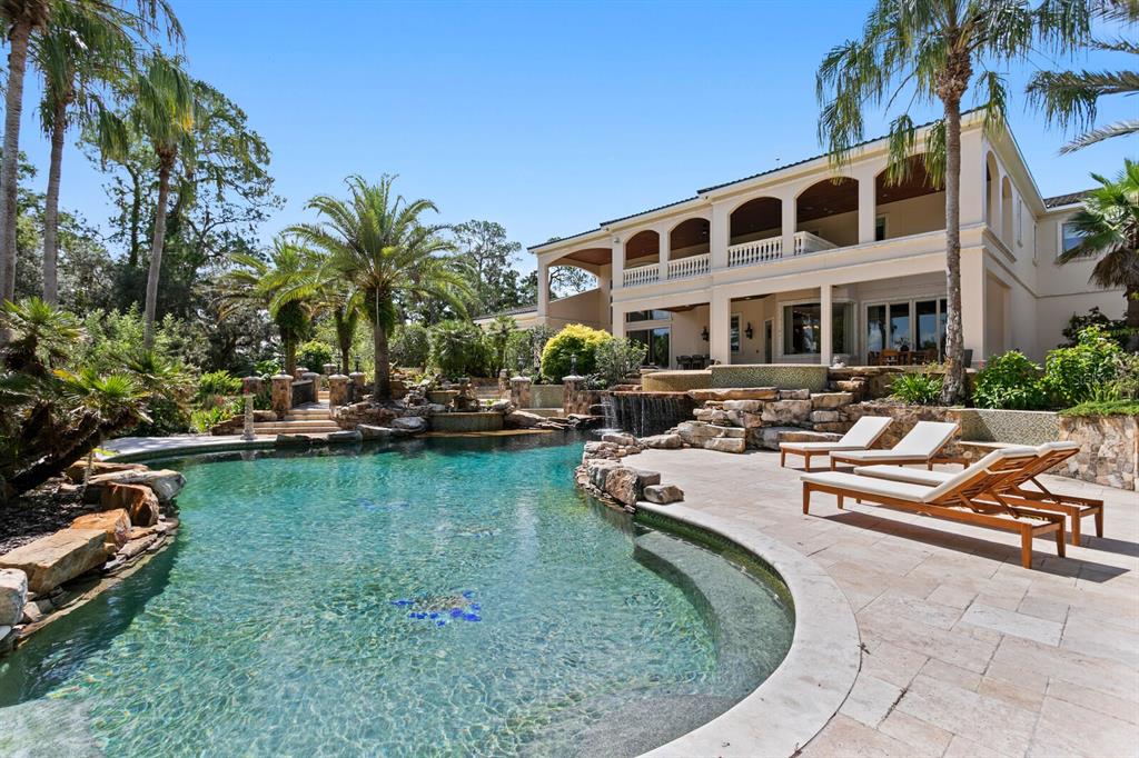 A two-story house features a large swimming pool with a rock waterfall and lounge chairs — 7850 FOUR PINES ROAD, PLANT CITY, FL