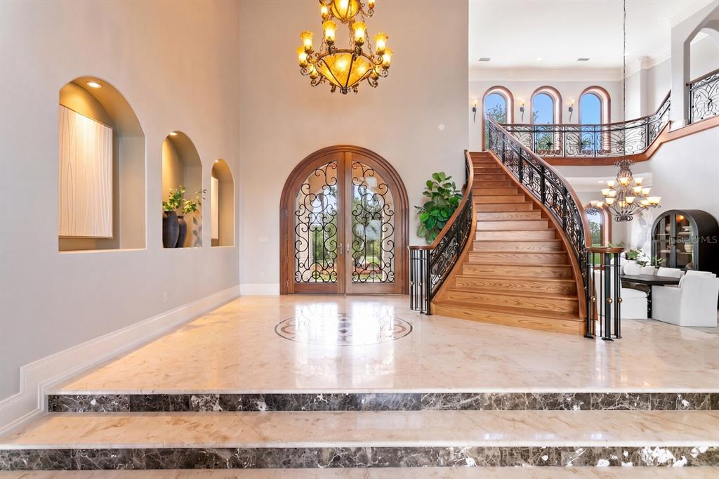 A grand foyer features a marble staircase, arched doorways, and a decorative wrought iron front door — 7850 FOUR PINES ROAD, PLANT CITY, FL