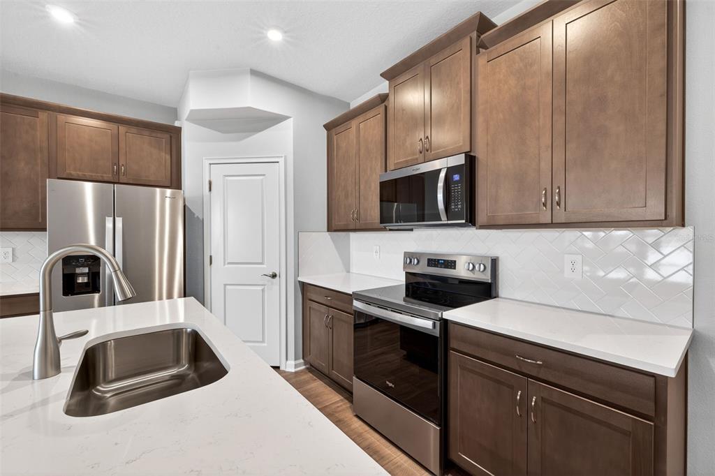 A kitchen features brown cabinets, stainless steel appliances, a white island, and a herringbone backsplash — 9187 AURELIA AVENUE, PARRISH, FL
