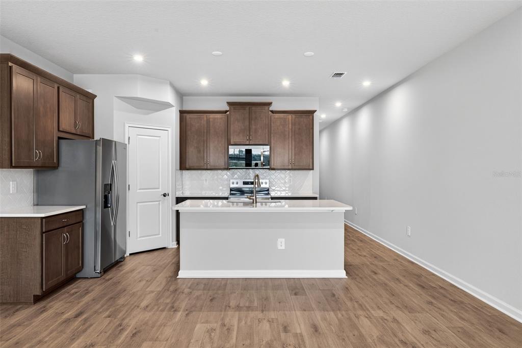 A kitchen features brown cabinets, stainless steel appliances, a white island, and wood-look flooring — 9187 AURELIA AVENUE, PARRISH, FL