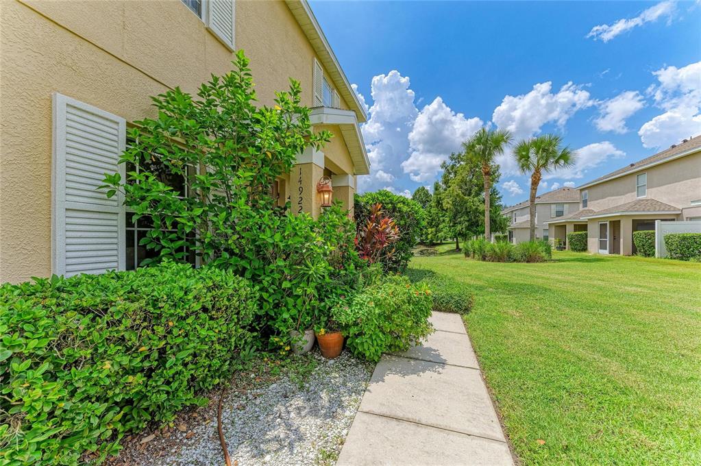 A side view of a tan house exterior with lush landscaping and a concrete walkway — 14922 AMBERJACK TERRACE UNIT 106, BRADENTON, FL