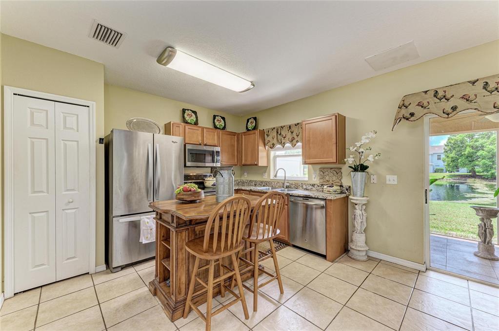 A kitchen with wood cabinets, stainless steel appliances, a center island, and a sliding glass door — 14922 AMBERJACK TERRACE UNIT 106, BRADENTON, FL