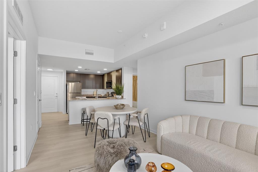 An open-concept living and dining area features a modern kitchen, light wood floors, and neutral furniture — 5579 MILLENIA PARK BOULEVARD UNIT 402, ORLANDO, FL