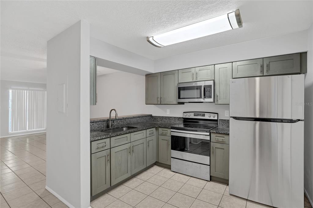 A kitchen features gray cabinets, granite countertops, stainless steel appliances, and light-colored tile flooring — 2801 WILLOW RUN, ORLANDO, FL