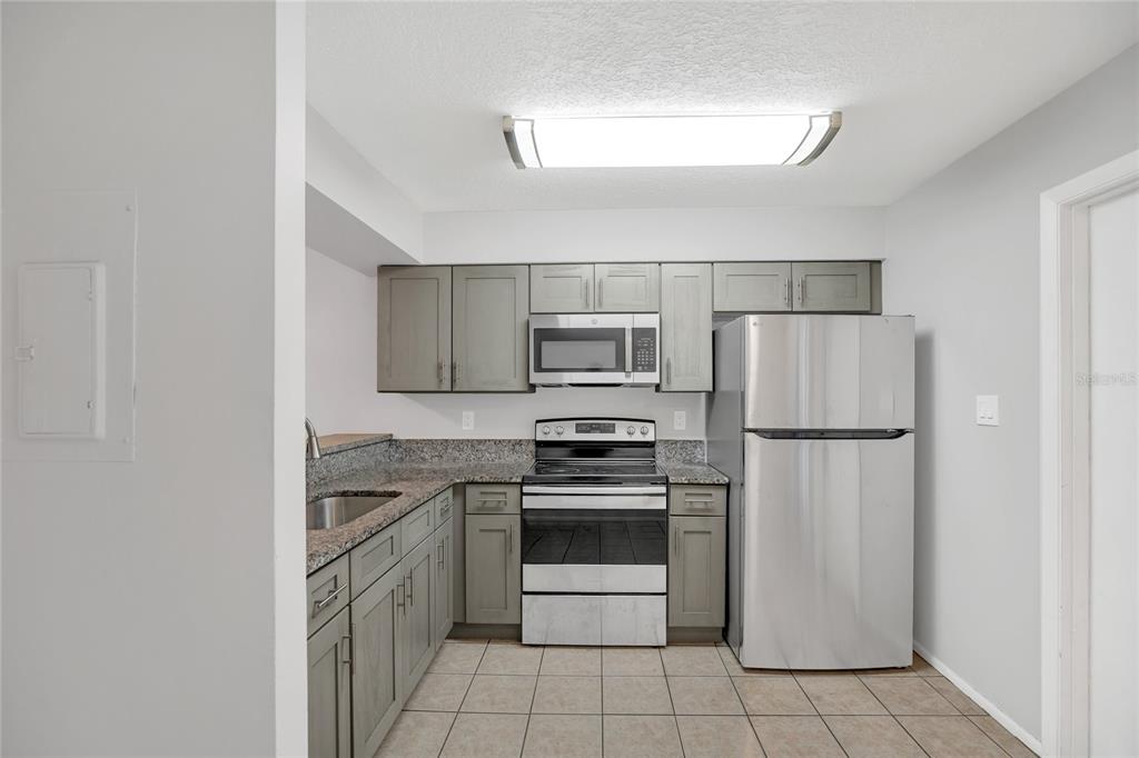 A kitchen features gray cabinets, stainless steel appliances, granite countertops, and light-colored tile flooring — 2801 WILLOW RUN, ORLANDO, FL