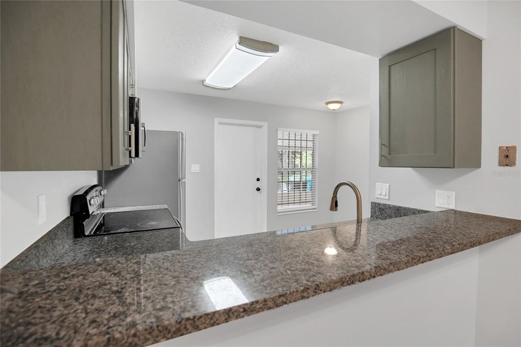 A kitchen with granite countertops, gray cabinets, and a view of a dining area — 2801 WILLOW RUN, ORLANDO, FL