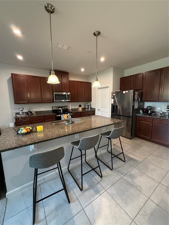 A kitchen features dark wood cabinets, granite countertops, a central island, and three bar stools — 1871 HOLDEN RIDGE LANE, MINNEOLA, FL