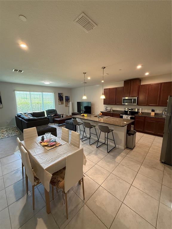 An open-concept kitchen and dining area features dark wood cabinets, granite countertops, and tile flooring — 1871 HOLDEN RIDGE LANE, MINNEOLA, FL
