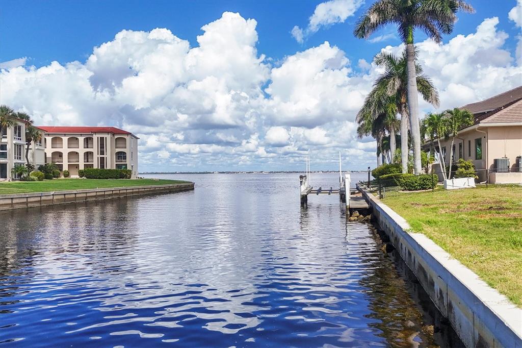 A canal leads toward a large body of water between a residential building and palms — 7 HIBISCUS DRIVE, PUNTA GORDA, FL