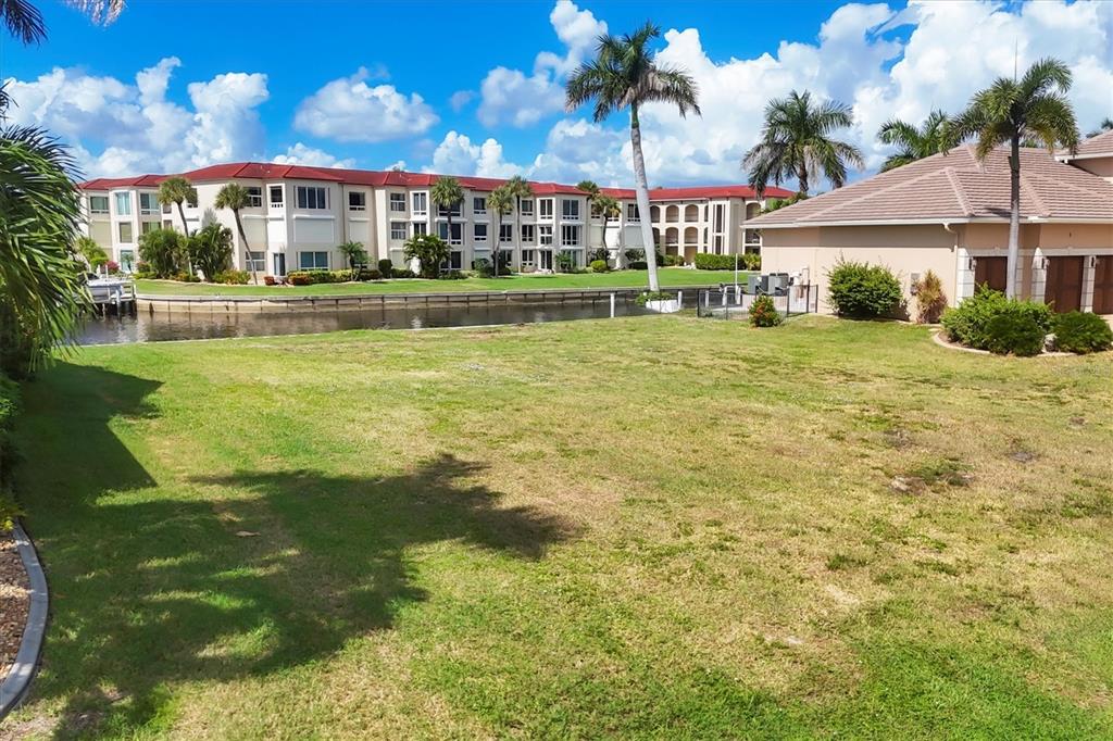 A grassy lawn overlooks a canal with a multi-story apartment building in the background — 7 HIBISCUS DRIVE, PUNTA GORDA, FL