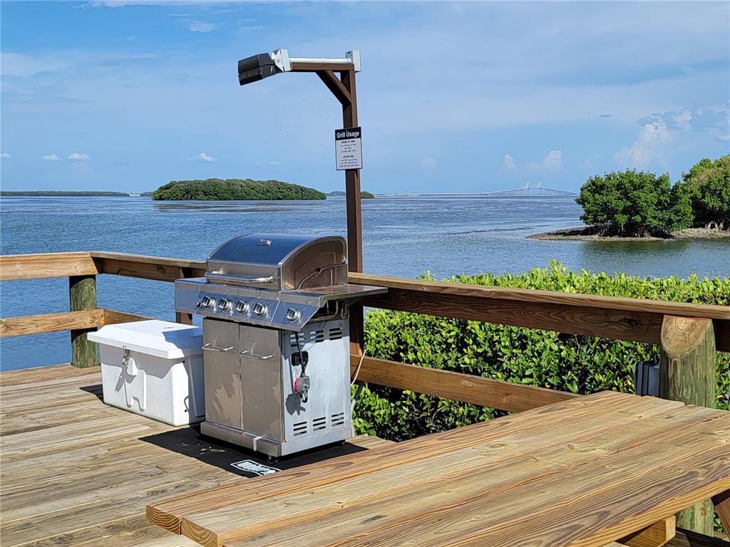A stainless steel grill sits on a wooden deck overlooking the water and a bridge — 1515 PINELLAS BAYWAY S UNIT 38, TIERRA VERDE, FL