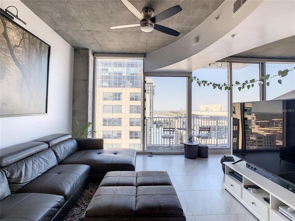 A modern living room features a leather sectional, concrete ceiling, and floor-to-ceiling windows with balcony — 155 S COURT AVENUE UNIT 1810, ORLANDO, FL