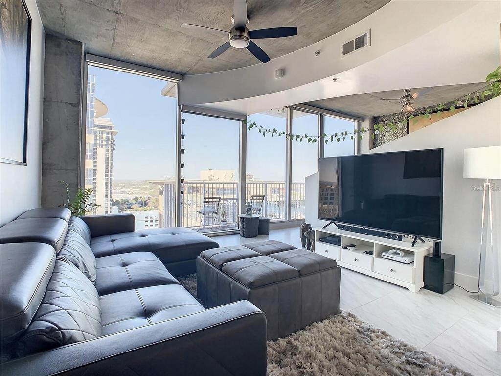 A modern living room features a gray sectional sofa, concrete ceiling, and floor-to-ceiling windows — 155 S COURT AVENUE UNIT 1810, ORLANDO, FL