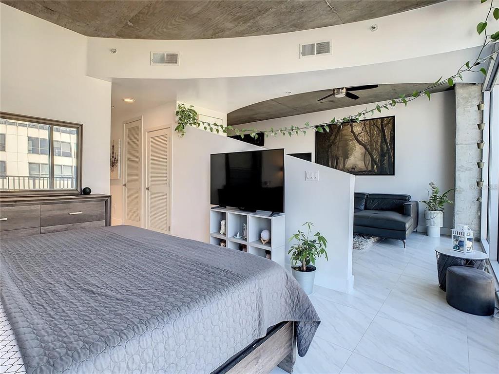 A bedroom with a concrete ceiling, a partial wall divider, and an adjacent seating area — 155 S COURT AVENUE UNIT 1810, ORLANDO, FL