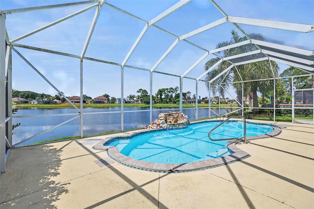 A screened-in swimming pool with a rock water feature overlooks a lake — 423 STONEHENGE CIRCLE, ROCKLEDGE, FL