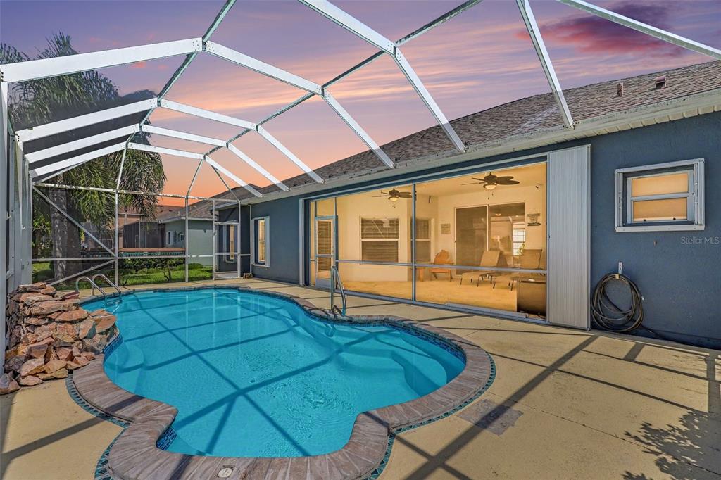 A swimming pool with a rock waterfall sits inside a screened-in patio area — 423 STONEHENGE CIRCLE, ROCKLEDGE, FL