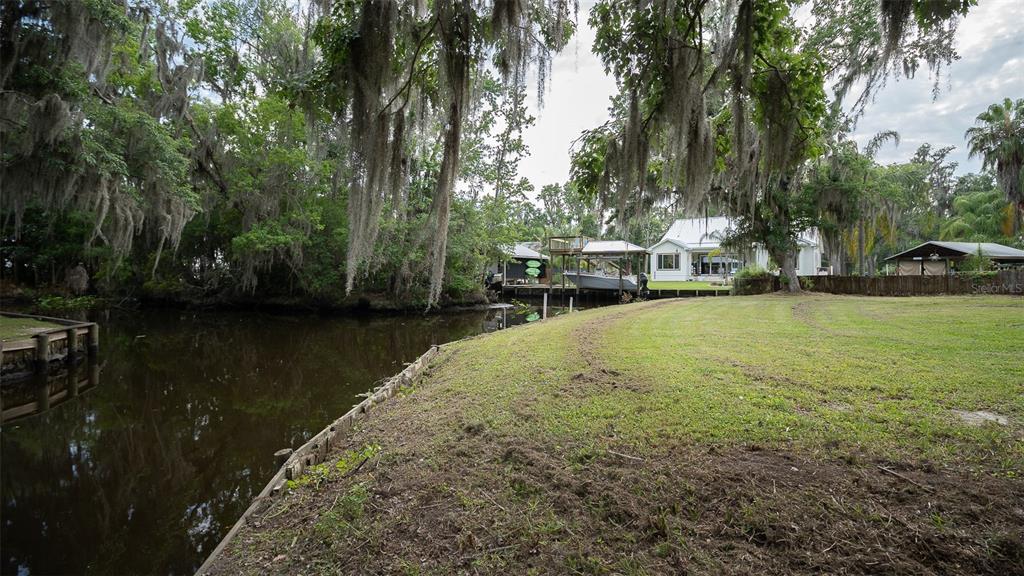 A grassy yard slopes down to a canal with a boat dock and overhanging trees — 8211 COLEE COVE BRANCH ROAD, ST AUGUSTINE, FL