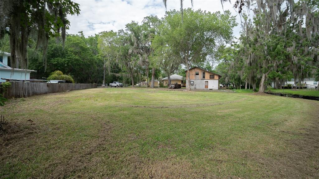 A large, grassy vacant lot with mature trees and a small house in the background — 8211 COLEE COVE BRANCH ROAD, ST AUGUSTINE, FL