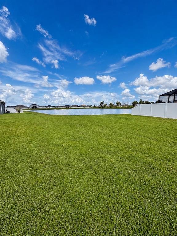 A grassy backyard overlooks a community pond under a blue sky with scattered clouds — 9589 SANDY BLUFFS CIRCLE, PARRISH, FL