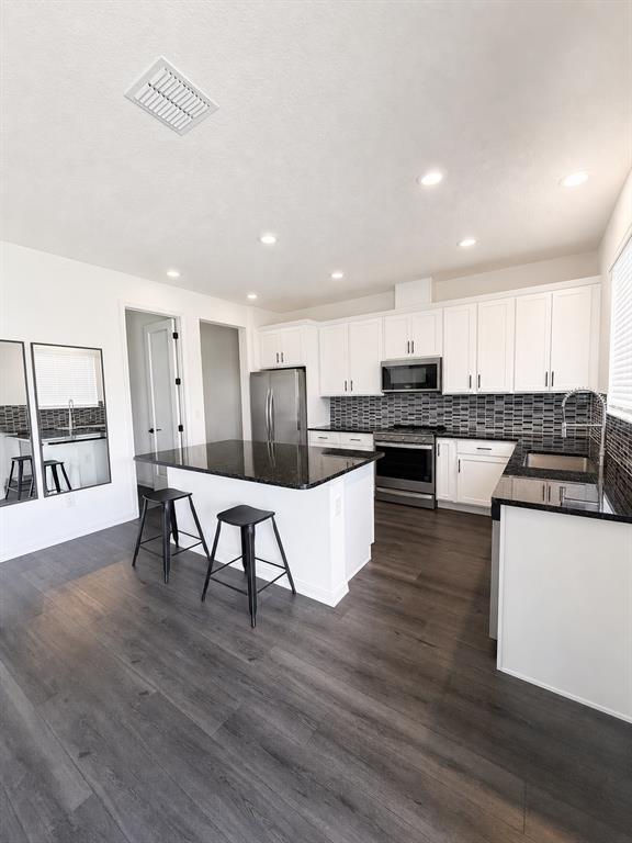 A modern kitchen features white cabinets, a dark granite island with stools, and wood-look flooring — 9589 SANDY BLUFFS CIRCLE, PARRISH, FL