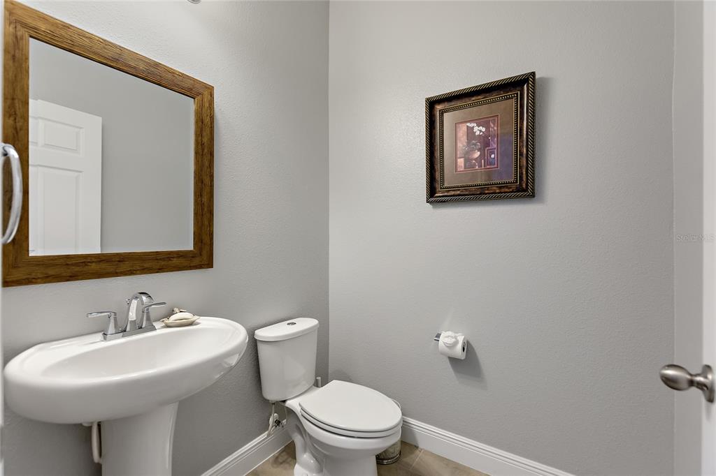A small bathroom features a pedestal sink, a toilet, and a framed mirror on gray walls — 8719 CRESCENDO AVENUE, WINDERMERE, FL