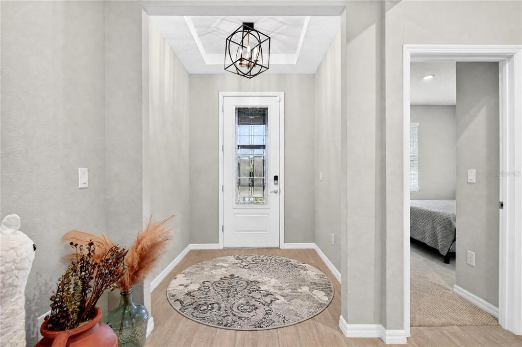 A bright entryway features light wood-look flooring, a round patterned rug, and a geometric pendant light — 3329 BIG SKY WAY, LAKEWOOD RANCH, FL